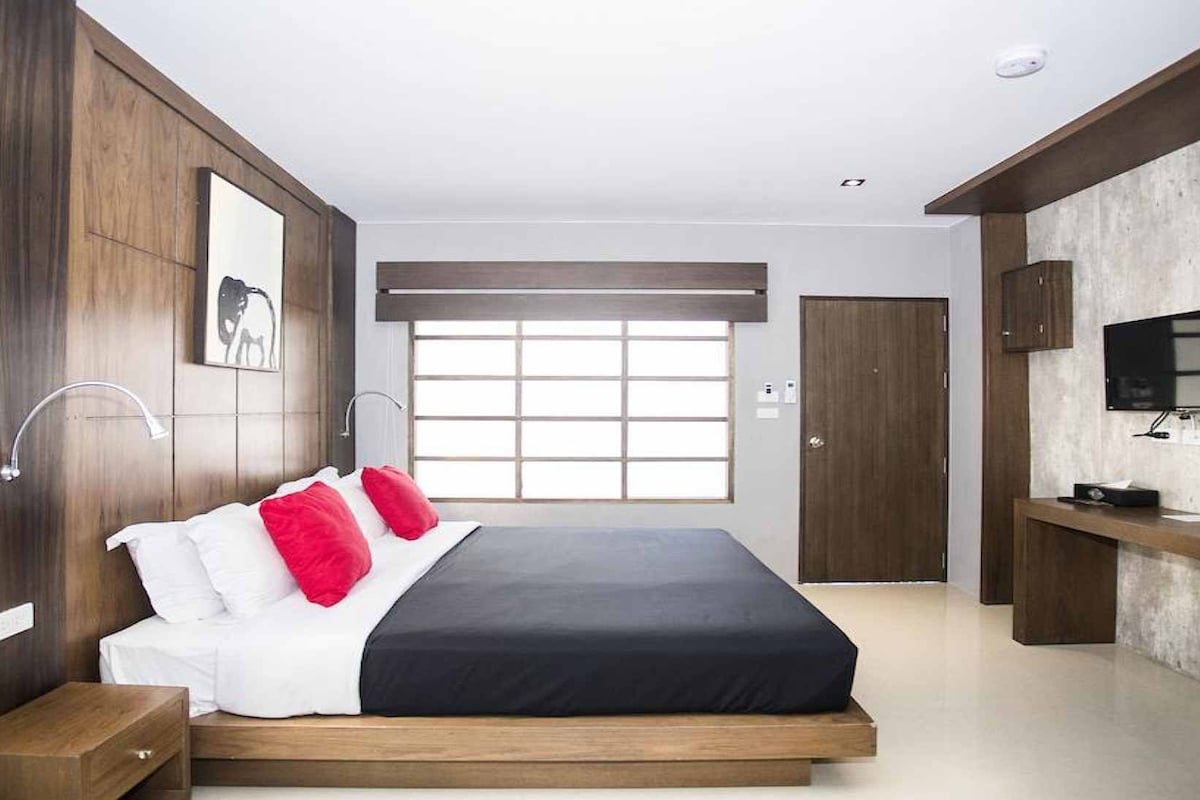 A modern bedroom with a large bed, wooden paneling, a TV, and a window.