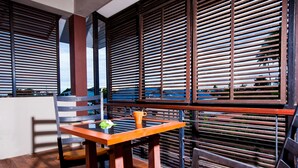 A modern outdoor seating area with a wooden table and chairs, a metal railing, and a view of the sky. - Amenity Apartel Samui (Koh Samui)