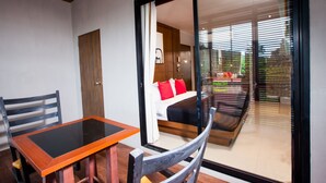 A room with a bed, a table, and a chair. There is a sliding glass door leading to a balcony. - Amenity Apartel Samui (Koh Samui)