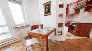 En matplats med ett träbord och vita stolar, ett fönster med persienner och ett kök med träskåp och en spis.