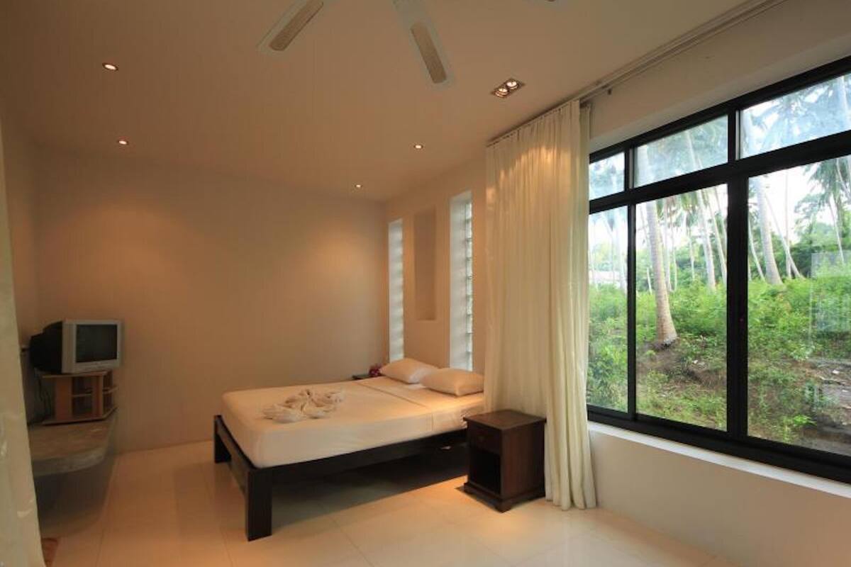 A bedroom with a bed, a TV, and a window with a view of greenery.