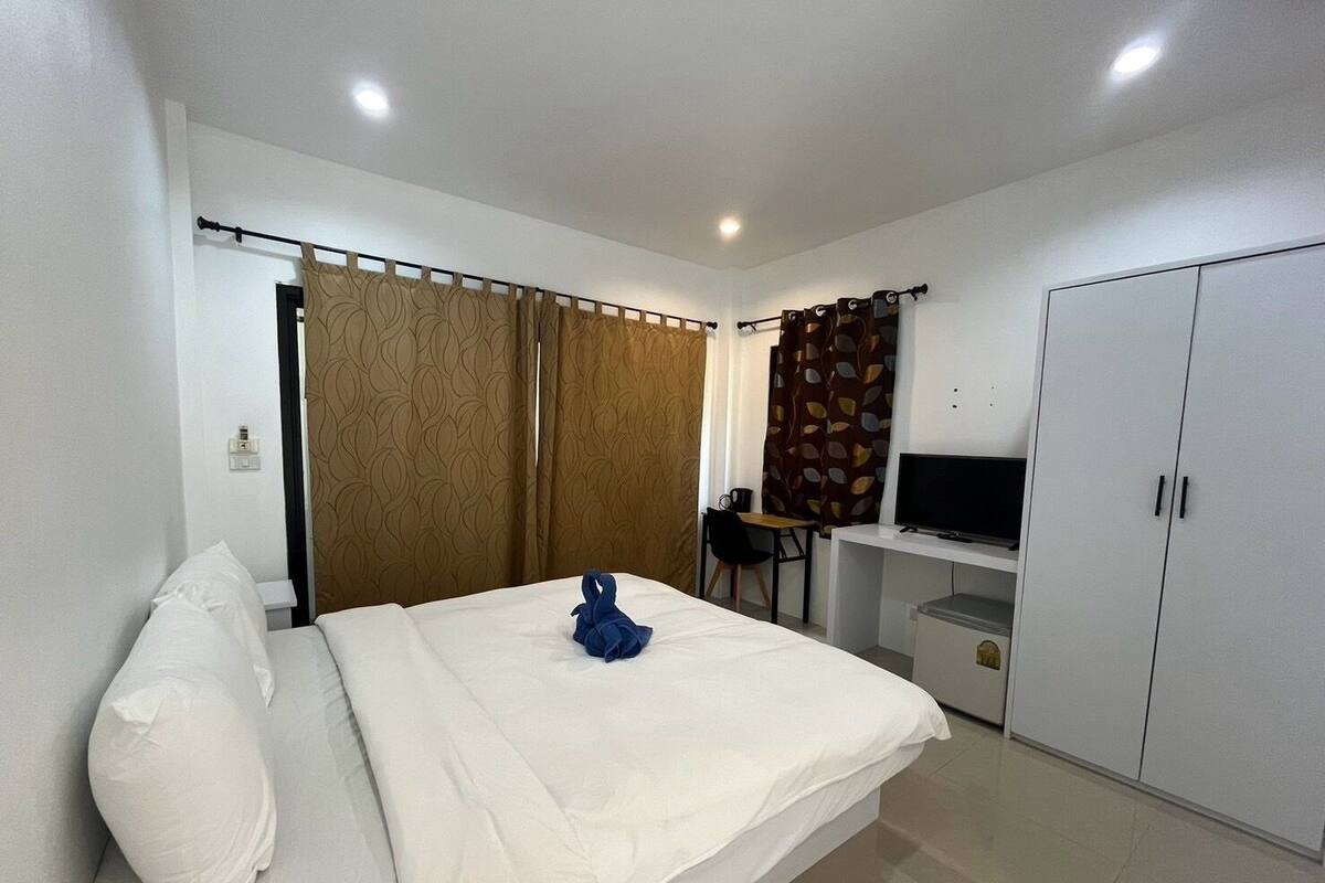 A hotel room with a bed, a desk with a chair, a television, and a wardrobe.