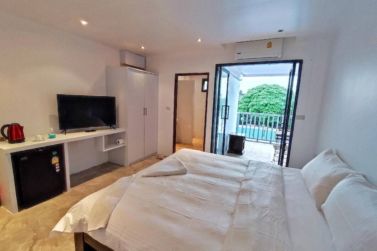 A bedroom with a bed, a TV on a stand, a wardrobe, and a balcony with a pool view.