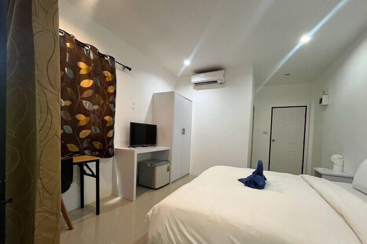 A bedroom with a bed, a desk with a television, a wardrobe, and an air conditioning unit.