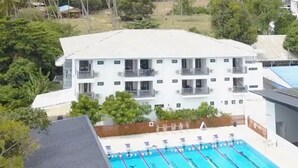 A multi-story building with balconies, a swimming pool with lanes, and a fenced area. - Superpro Samui (Koh Samui)