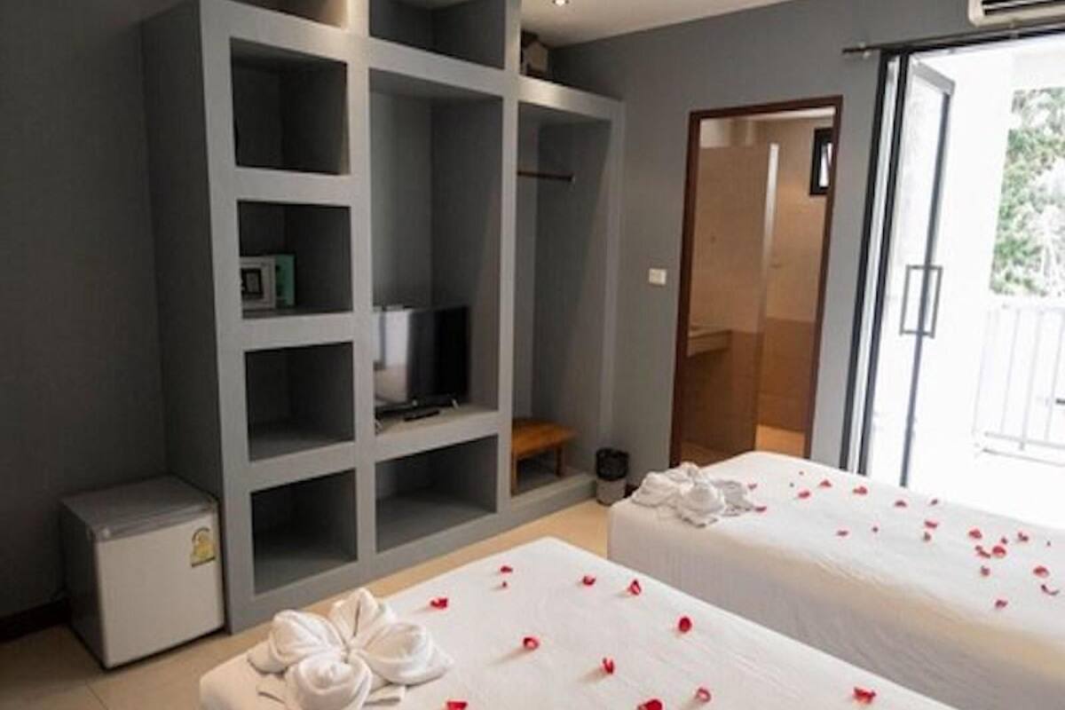 A hotel room with two beds, a minibar, a TV, and a sliding glass door to the outside.