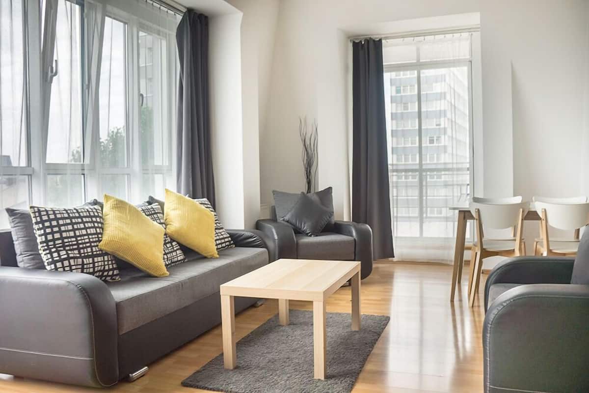 A modern living room with a grey sofa, a wooden coffee table, and a dining area with white chairs.