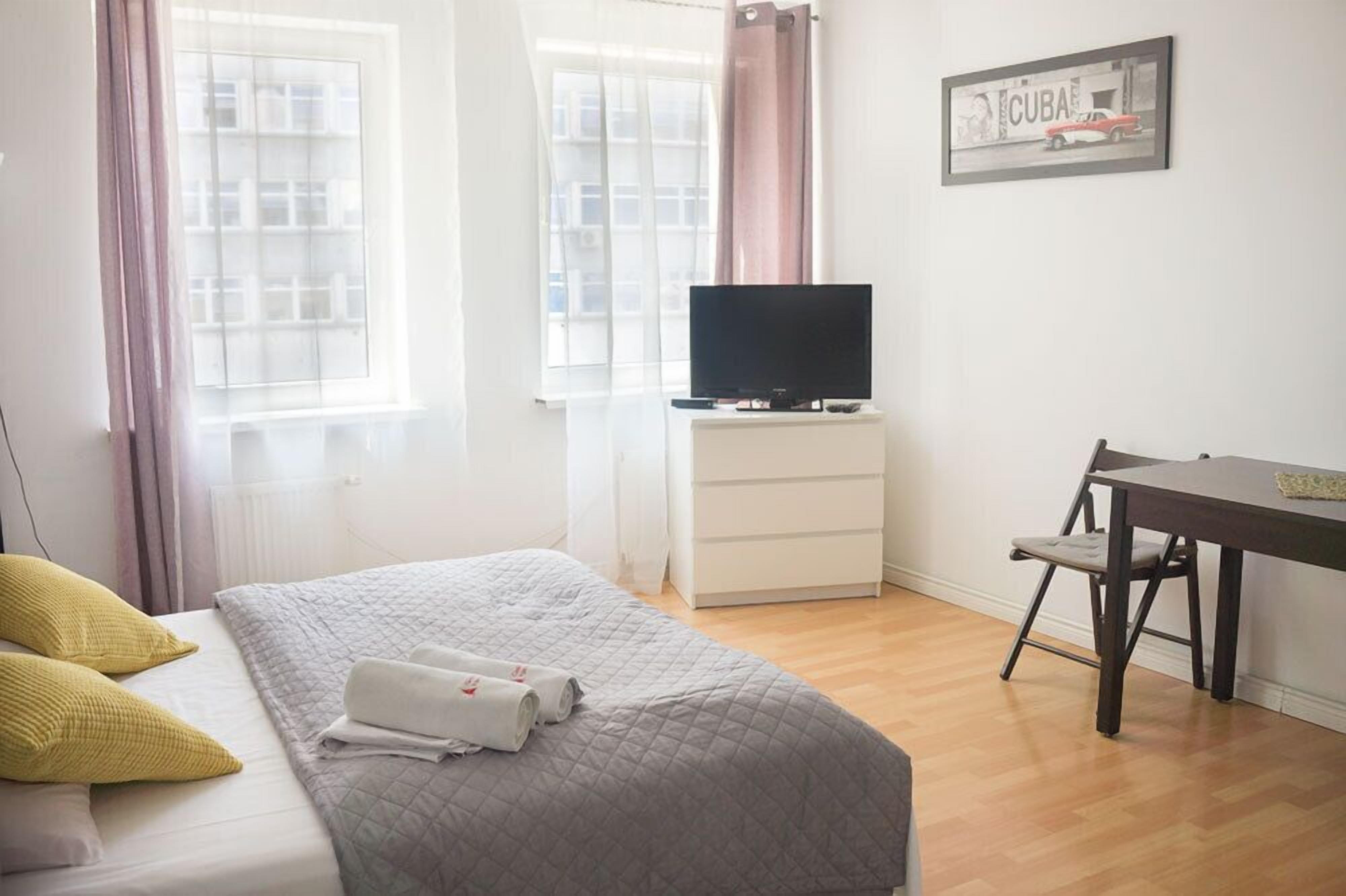Habitación de hotel con cama, televisor en una cómoda, mesa de comedor con una silla y ventana con cortinas.
