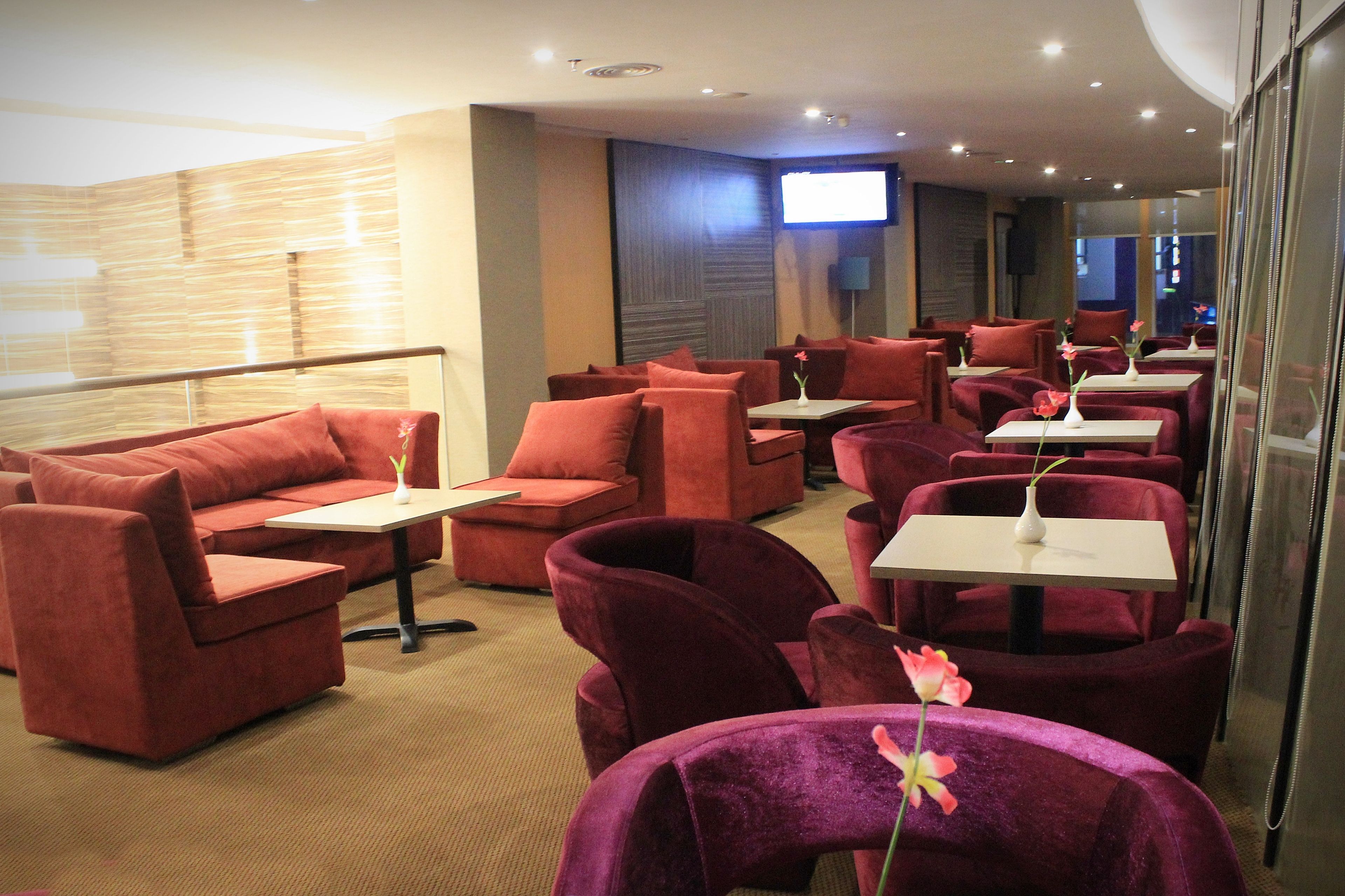 A hotel lobby with red sofas and chairs, small tables, and a TV on the wall.