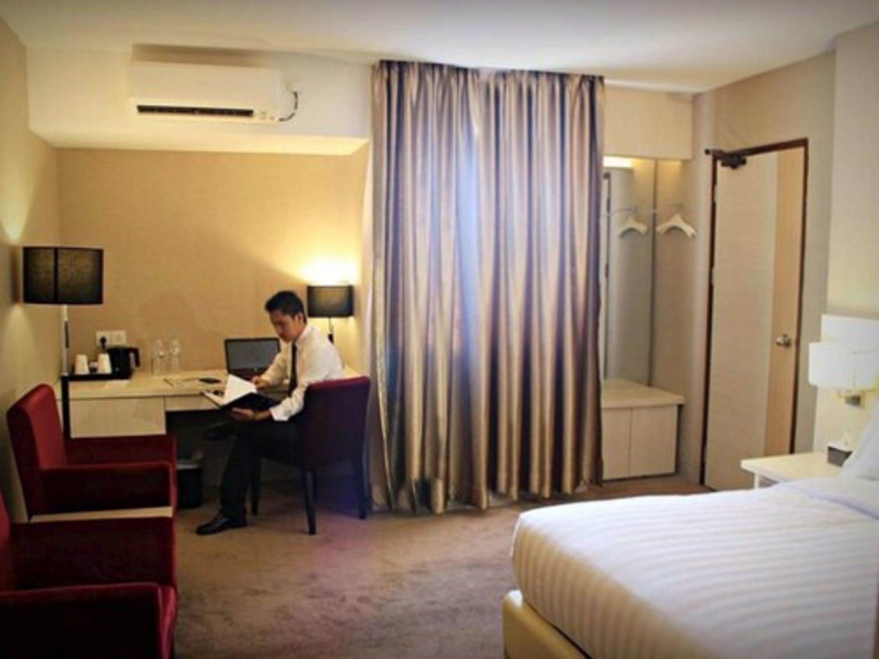 Une chambre d’hôtel comprenant un lit, un bureau avec un ordinateur, une chaise, une lampe de bureau, une armoire et un espace douche.