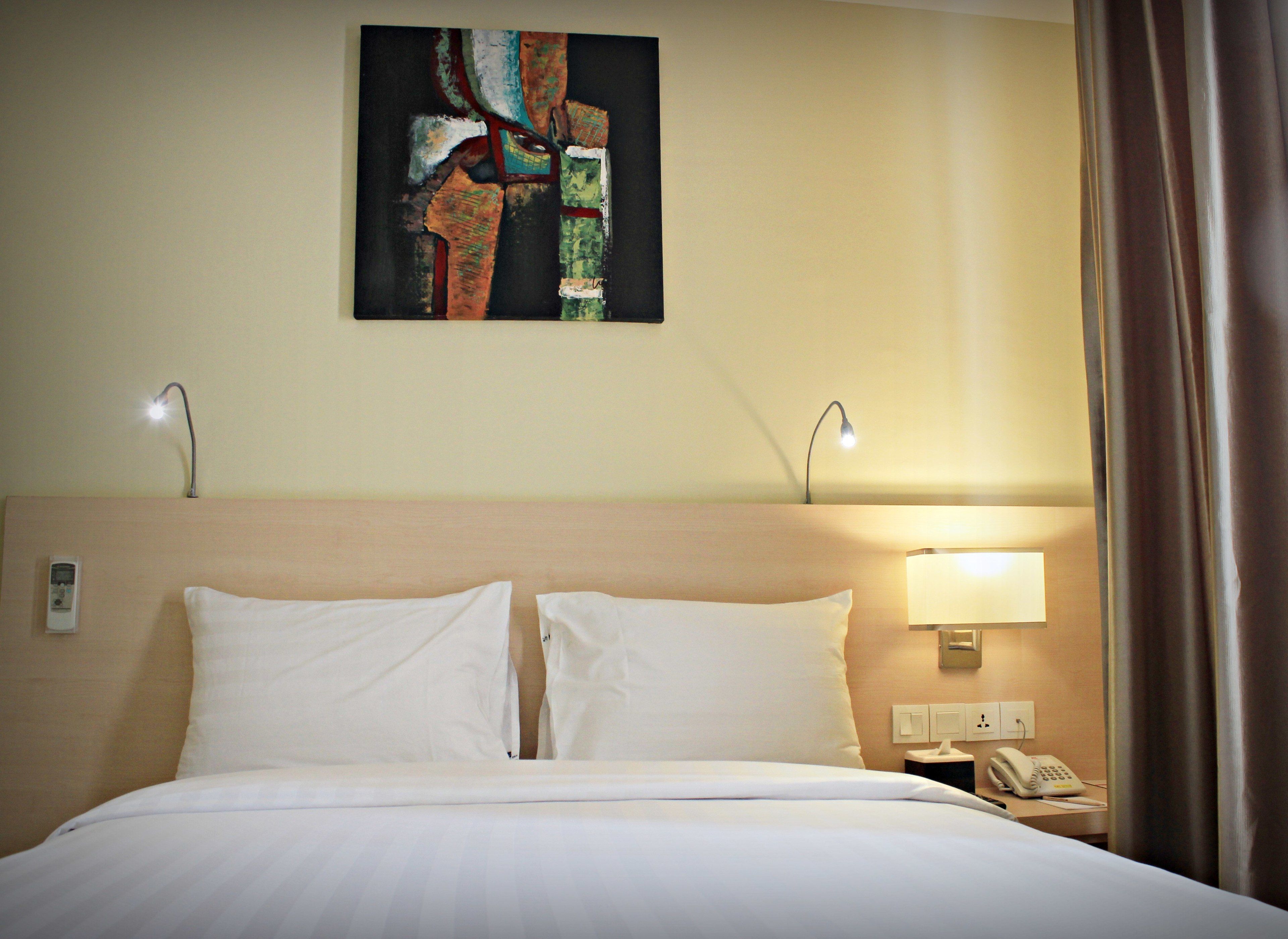 Una habitación de hotel con una cama, dos lámparas de noche, una mesita de noche con un teléfono y un cuadro en la pared.