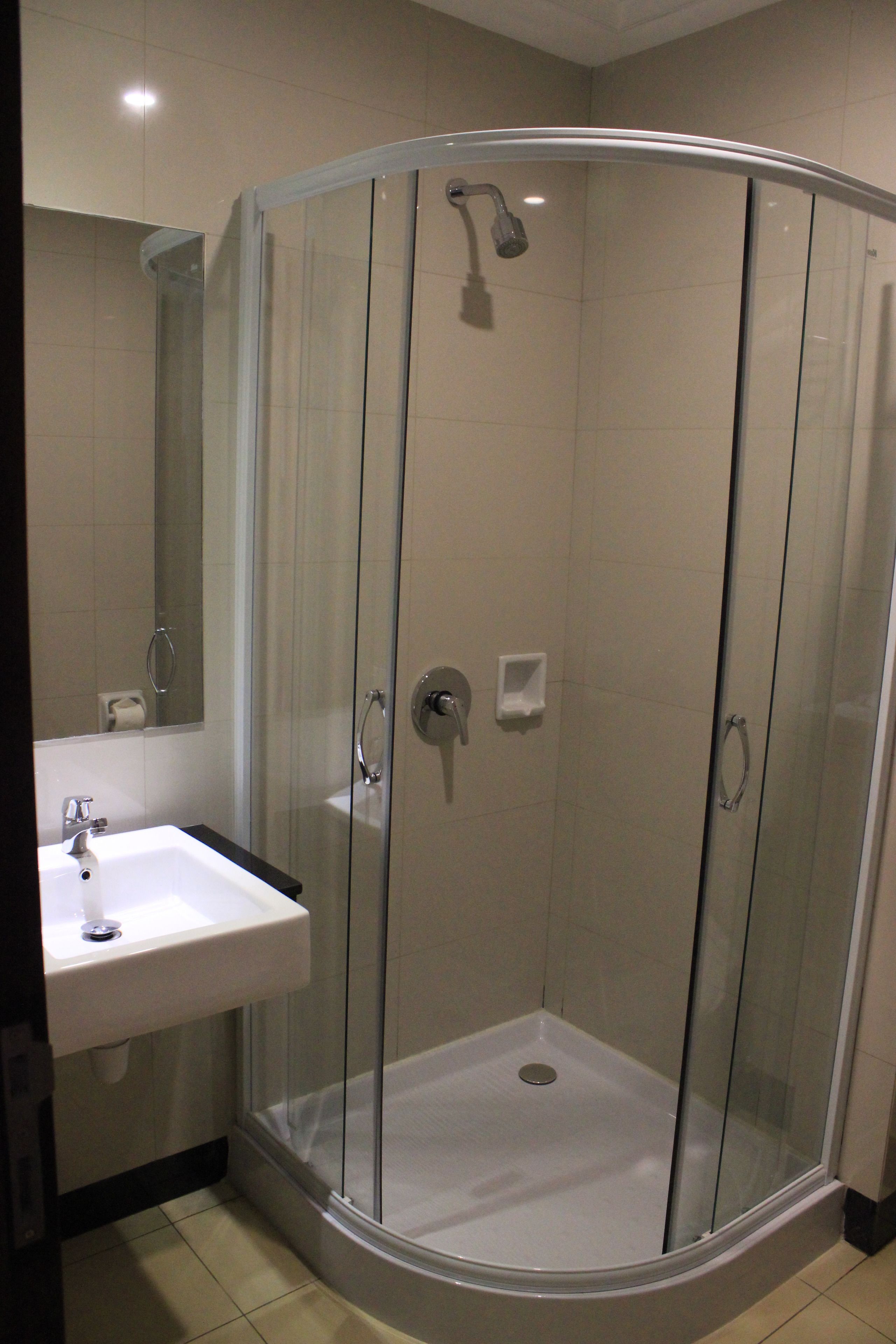 A modern bathroom with a glass-enclosed shower, a white sink, and a mirror.