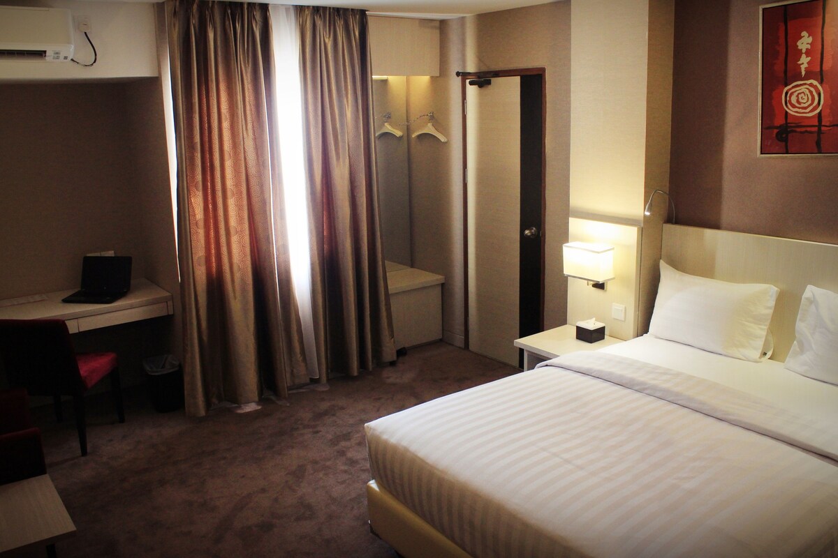 A hotel room with a bed, desk, chair, and a wardrobe.