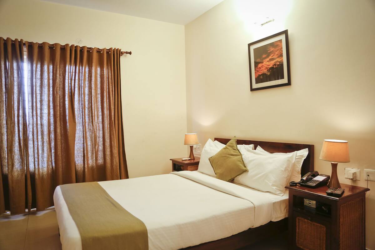A hotel room with a bed, two bedside tables, a lamp, a telephone, and a framed picture on the wall.