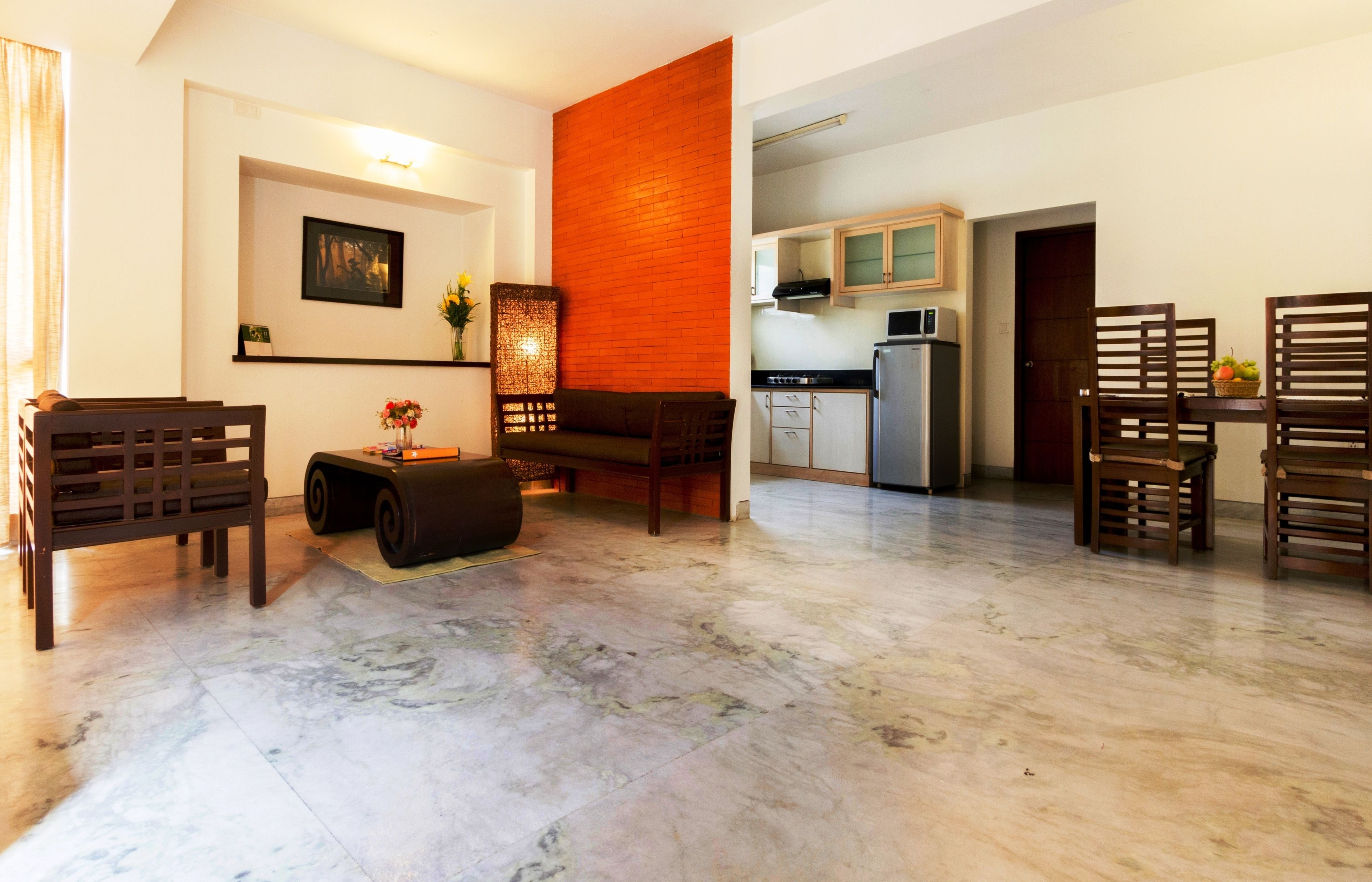 A living room with a sofa, a coffee table, and a dining area with chairs and a table. There is a kitchen area with cabinets and a refrigerator.