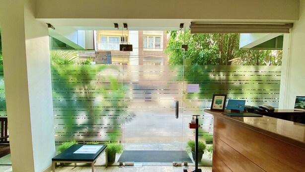 A reception area with a wooden desk, a small table with a plant, and a glass door leading outside. - Maple Suites Serviced Apartments (Bengaluru)
