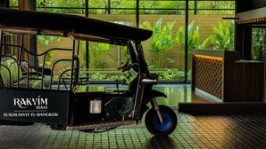Un tuk-tuk estacionado dentro de un edificio con amplios ventanales que dan a un jardín.