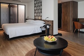 A modern hotel room with a large bed, a round table with fruit, a desk with a phone, and a wardrobe. - RakYim Siam - Sukhumvit 15 (Bangkok)