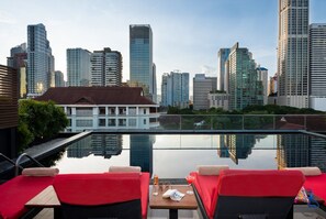 A rooftop pool with red lounge chairs and a table, overlooking a cityscape with modern high-rise buildings. - RakYim Siam - Sukhumvit 15 (Bangkok)