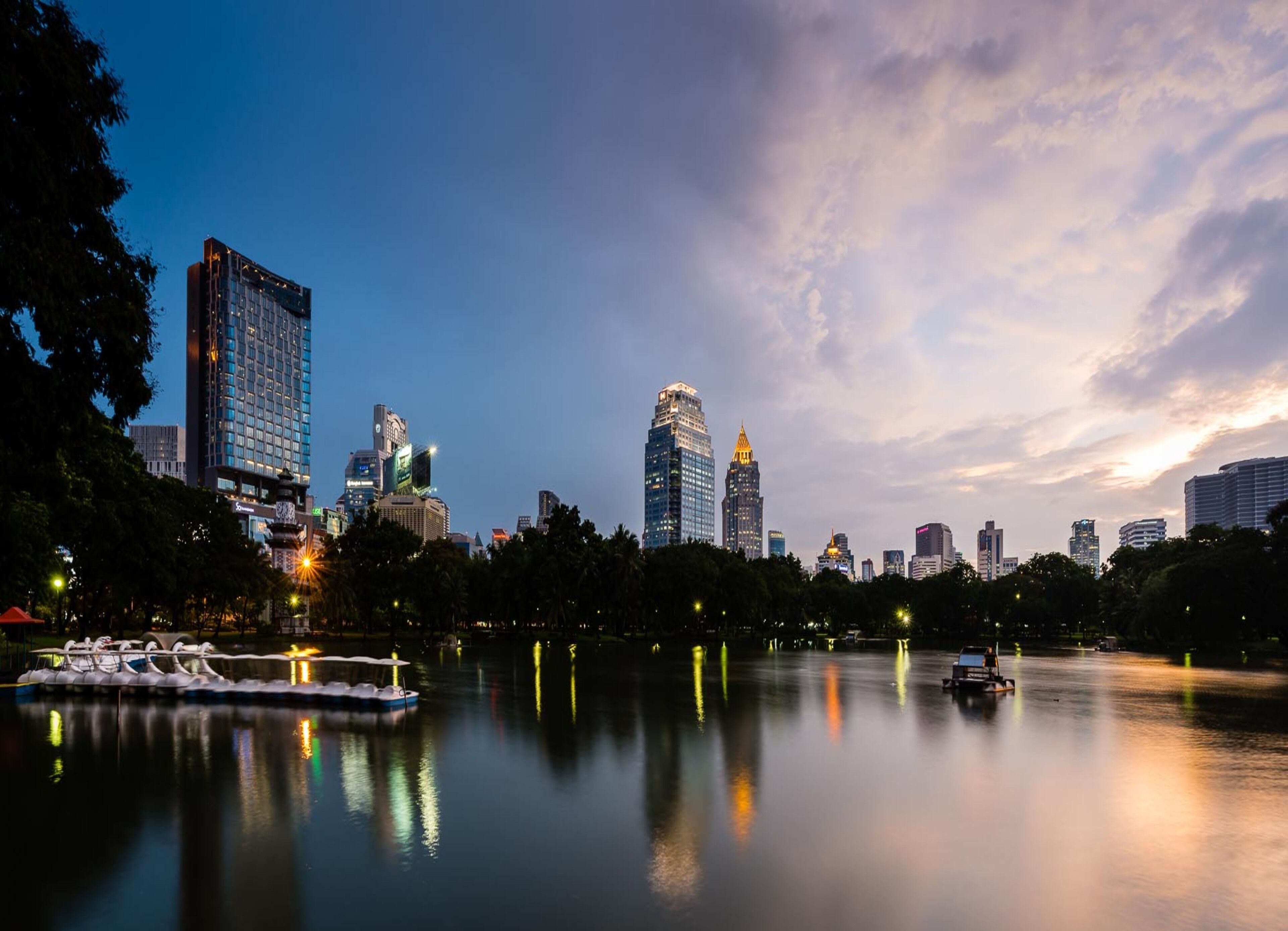 A city skyline at dusk with illuminated buildings reflecting on a calm river.