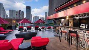 Un bar en la azotea con sombrillas rojas, asientos y vistas del horizonte urbano.