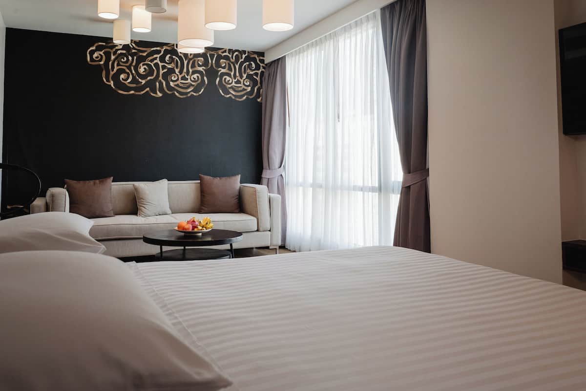 A modern hotel room with a large bed, a sofa, a coffee table with fruit, and a decorative wall piece.