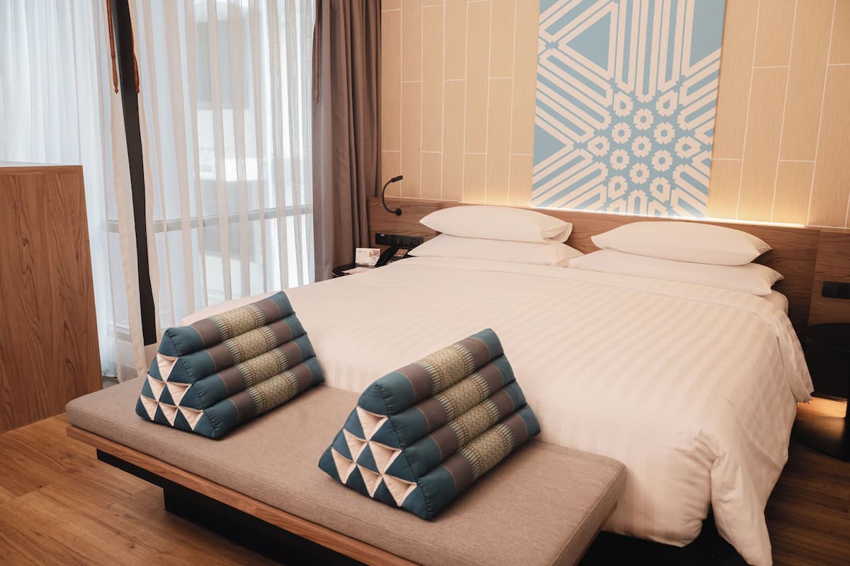 A modern hotel room with a large bed, a bedside table, and a bench with pillows.
