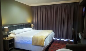 A hotel room with a bed, nightstands, a lamp, and a large window with curtains. - Sangiro Game Lodge (Bloemfontein)