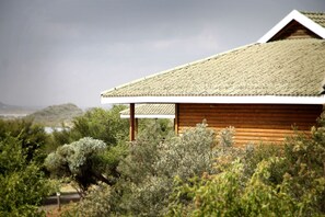 A wooden cabin with a sloped roof, surrounded by dense shrubbery and trees. - Sangiro Game Lodge (Bloemfontein)