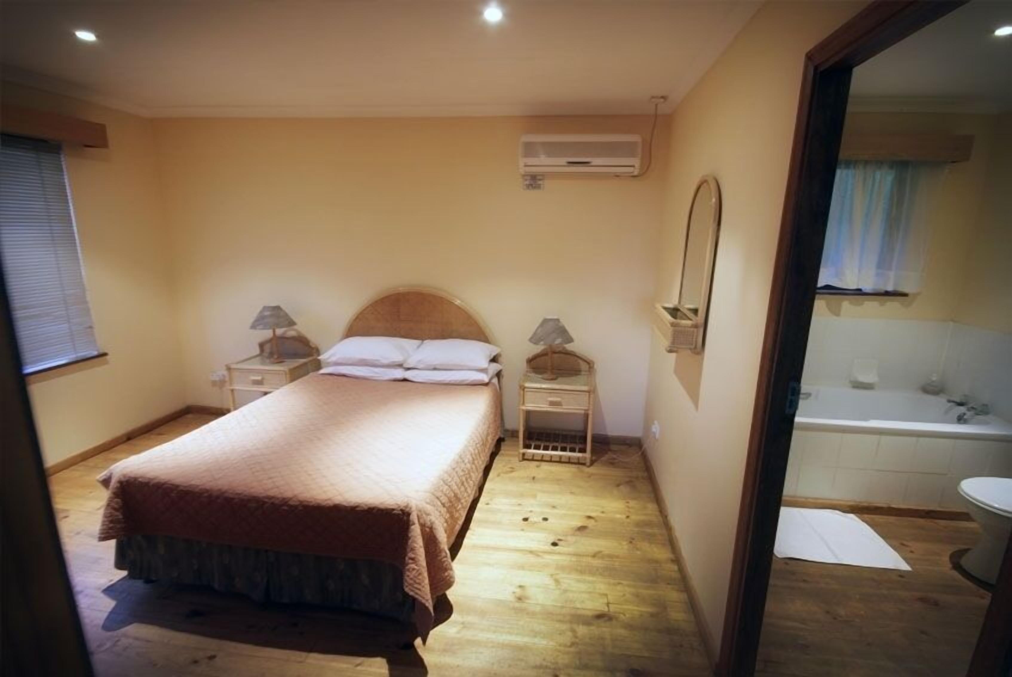 A bedroom with a bed, bedside tables, an air conditioner, and a view of a bathroom with a bathtub.