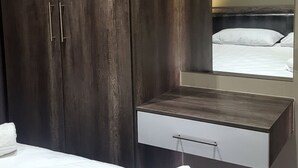Un dormitorio moderno con un armario grande, una mesita de noche y un espejo que refleja una cama.