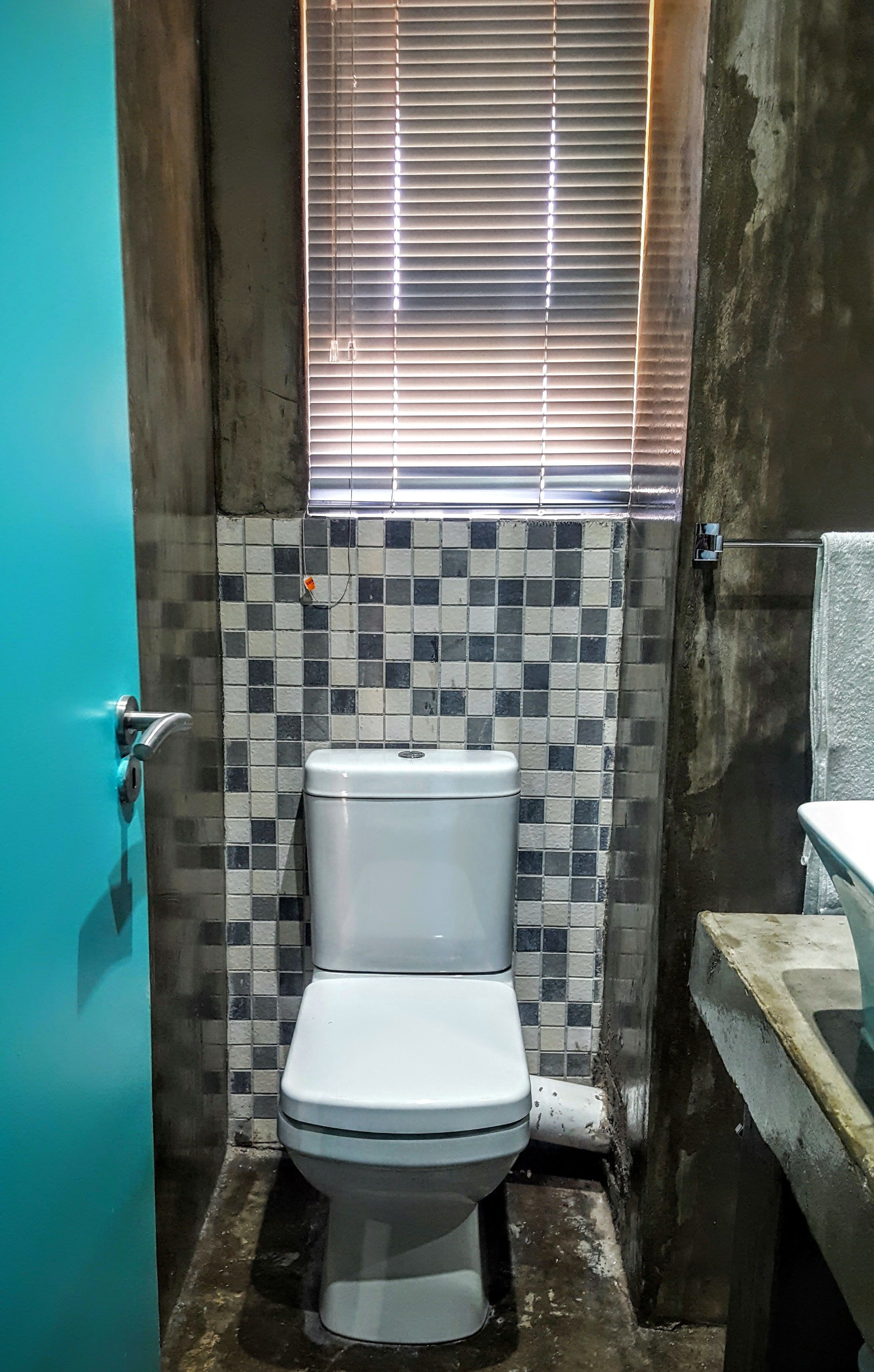 A small bathroom with a white toilet, tiled walls, and a window with blinds.