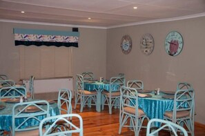 A dining area with round tables and chairs, a window with blinds, and three wall clocks. - Sangiro Game Lodge (Bloemfontein)