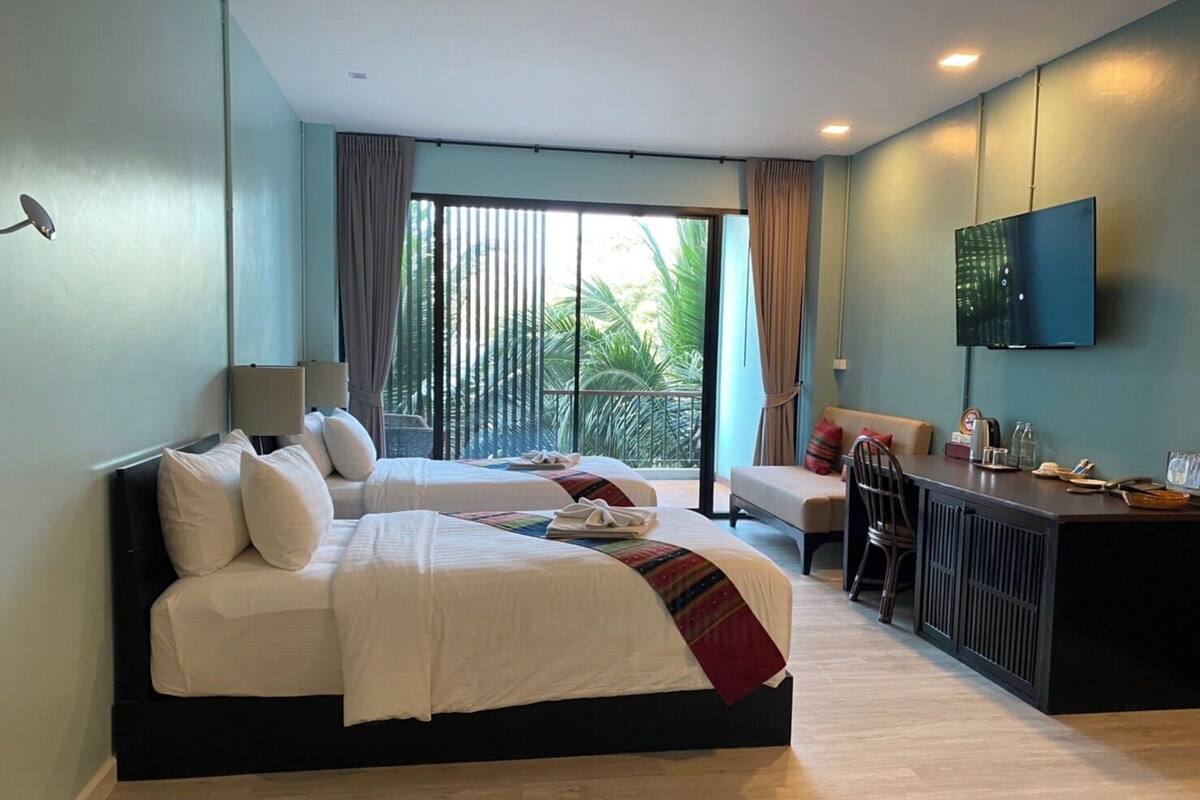 Une chambre d’hôtel avec un grand lit, un bureau avec une chaise, une télévision et un balcon avec des rideaux.