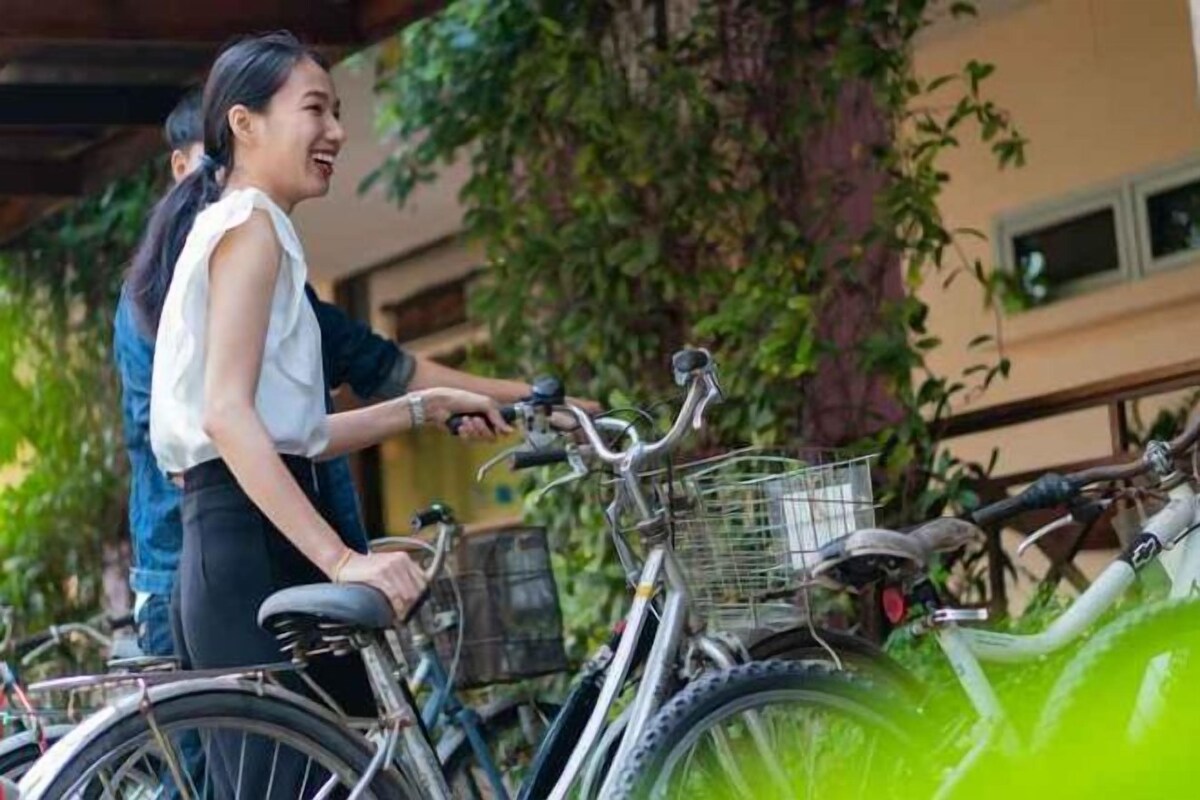 Une personne se tient à côté d’un vélo muni d’un panier, qui est garé à l’extérieur, avec de la verdure en arrière-plan.