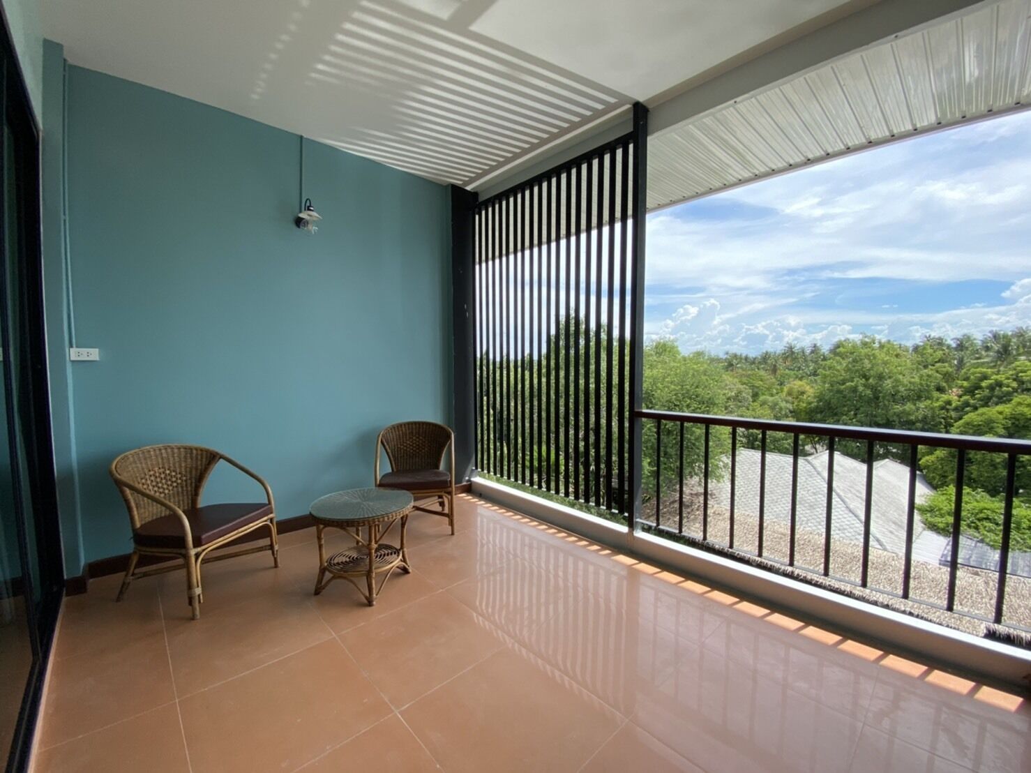 A balcony with two wicker chairs and a small table, a view of greenery and buildings, and a tiled floor.