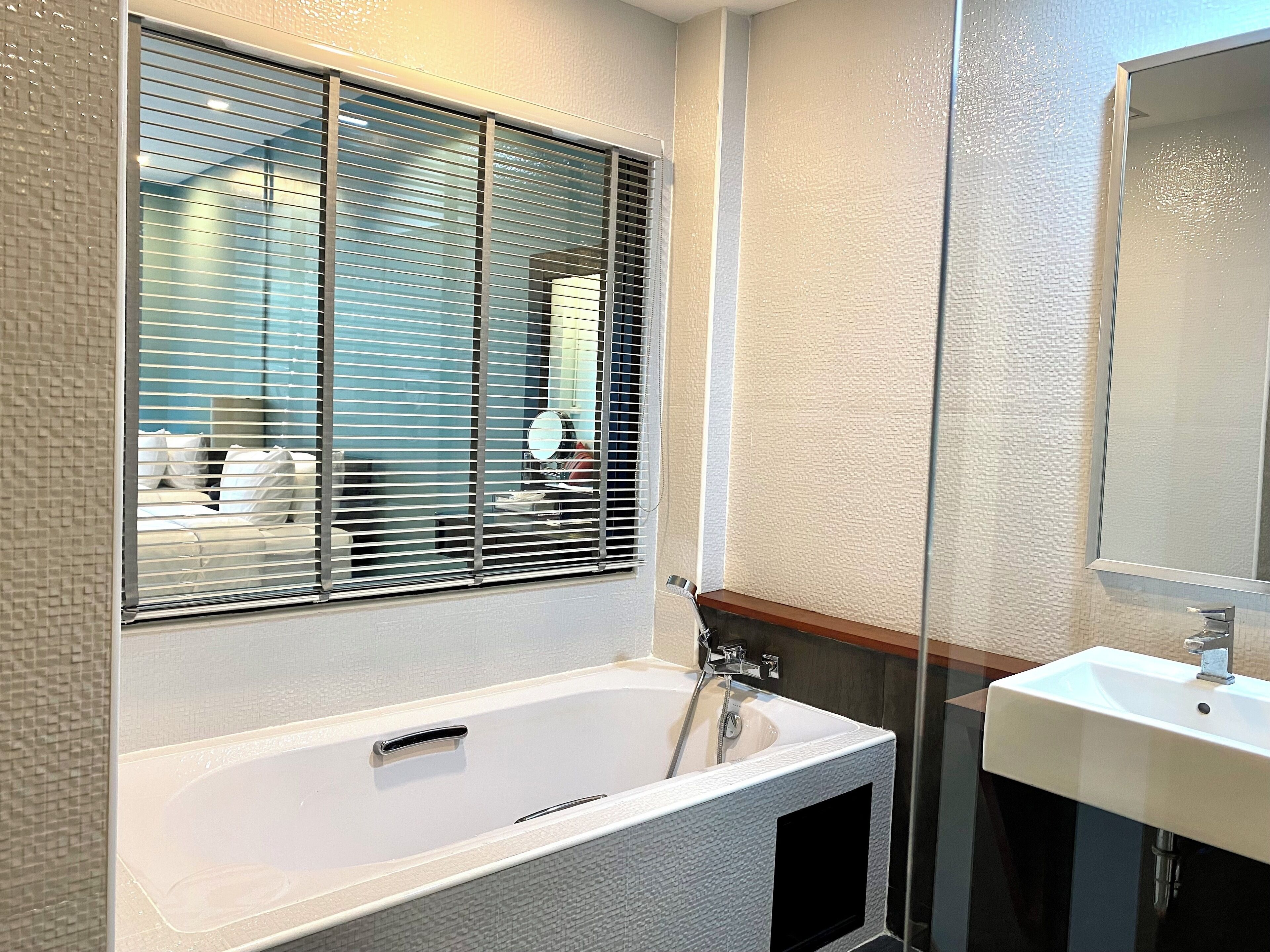 A modern bathroom with a large bathtub, a sink, and a window with blinds.