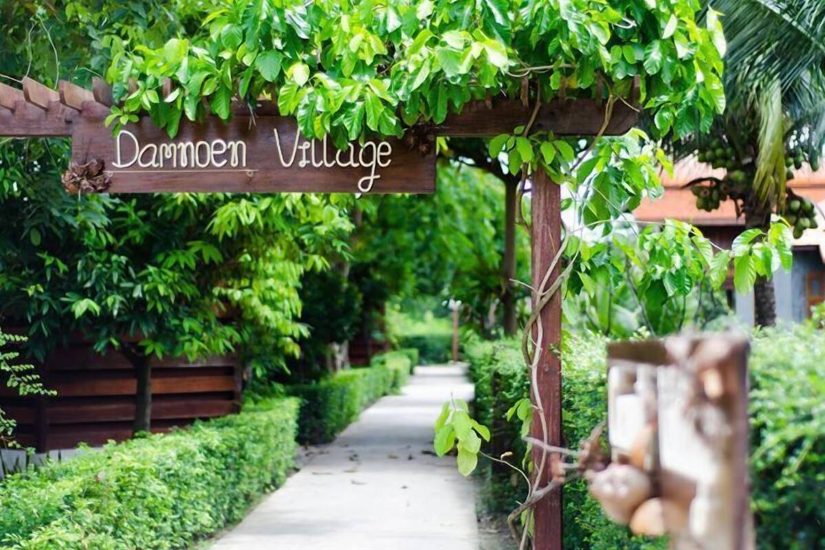 Une pergola en bois, sur laquelle on peut lire l’inscription « Village de Dammoen », se dresse au milieu d’une végétation luxuriante, à côté d’un sentier.