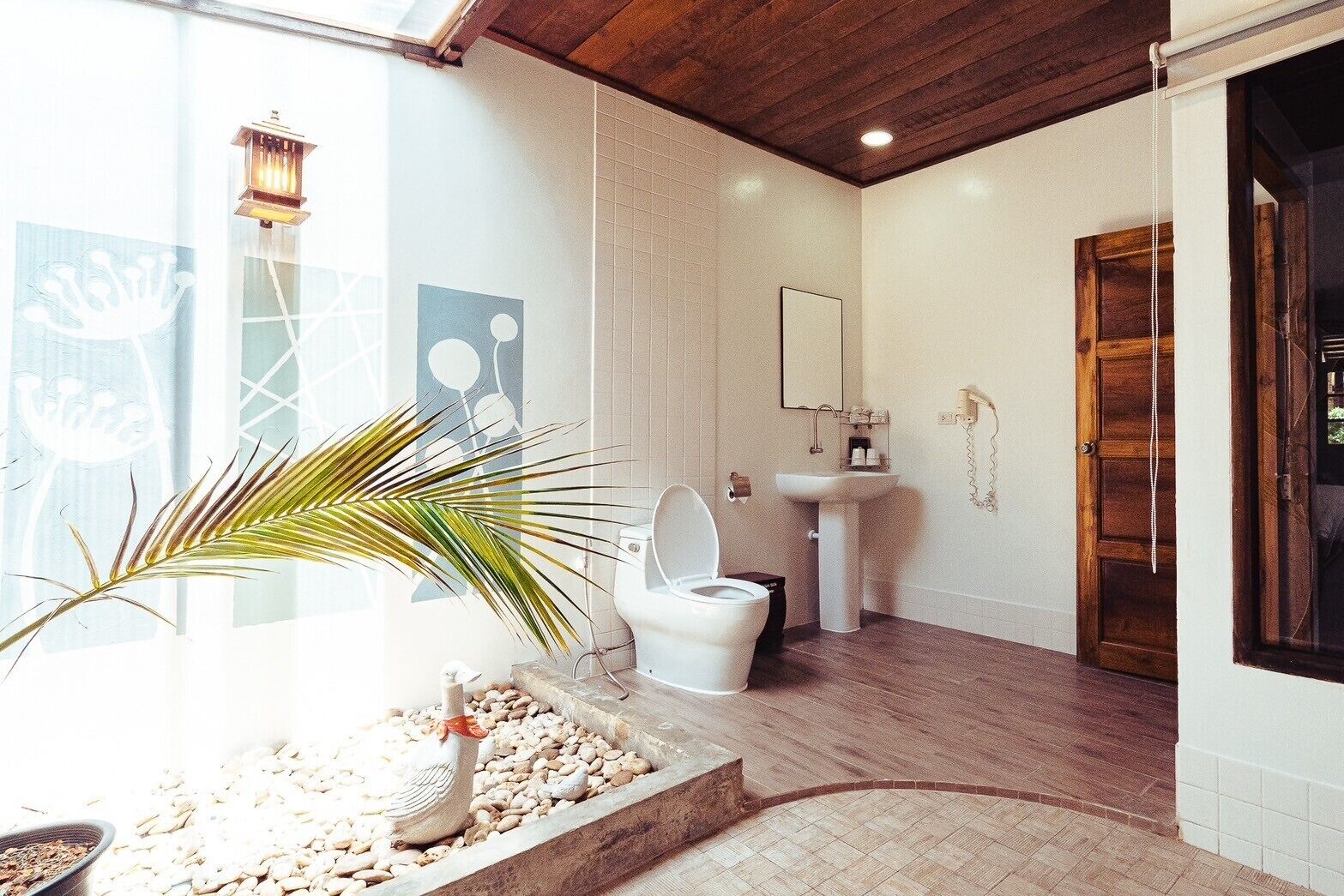 A bathroom with a white toilet, a sink, a wooden door, and a decorative plant.