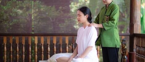 A person receiving a massage on a wooden massage table with a wooden railing in the background.