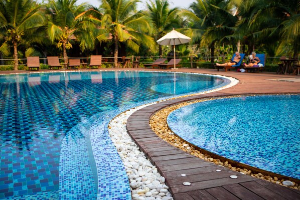 Piscina con borde de azulejos, rodeada de palmeras y sillas de descanso.