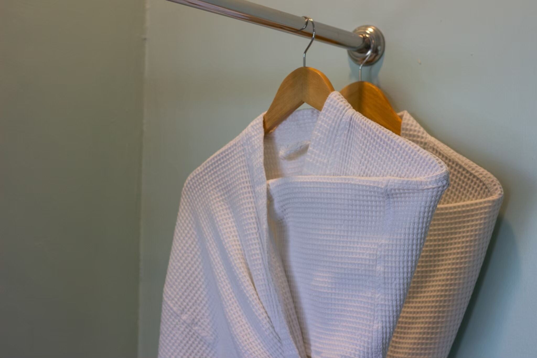 A white bathrobe hanging on a metal rod in a bathroom.