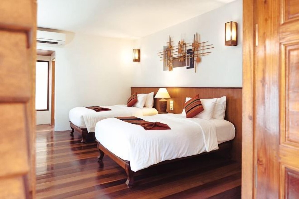 A hotel room with two beds, wooden flooring, a wall-mounted light fixture, and a decorative wall piece.