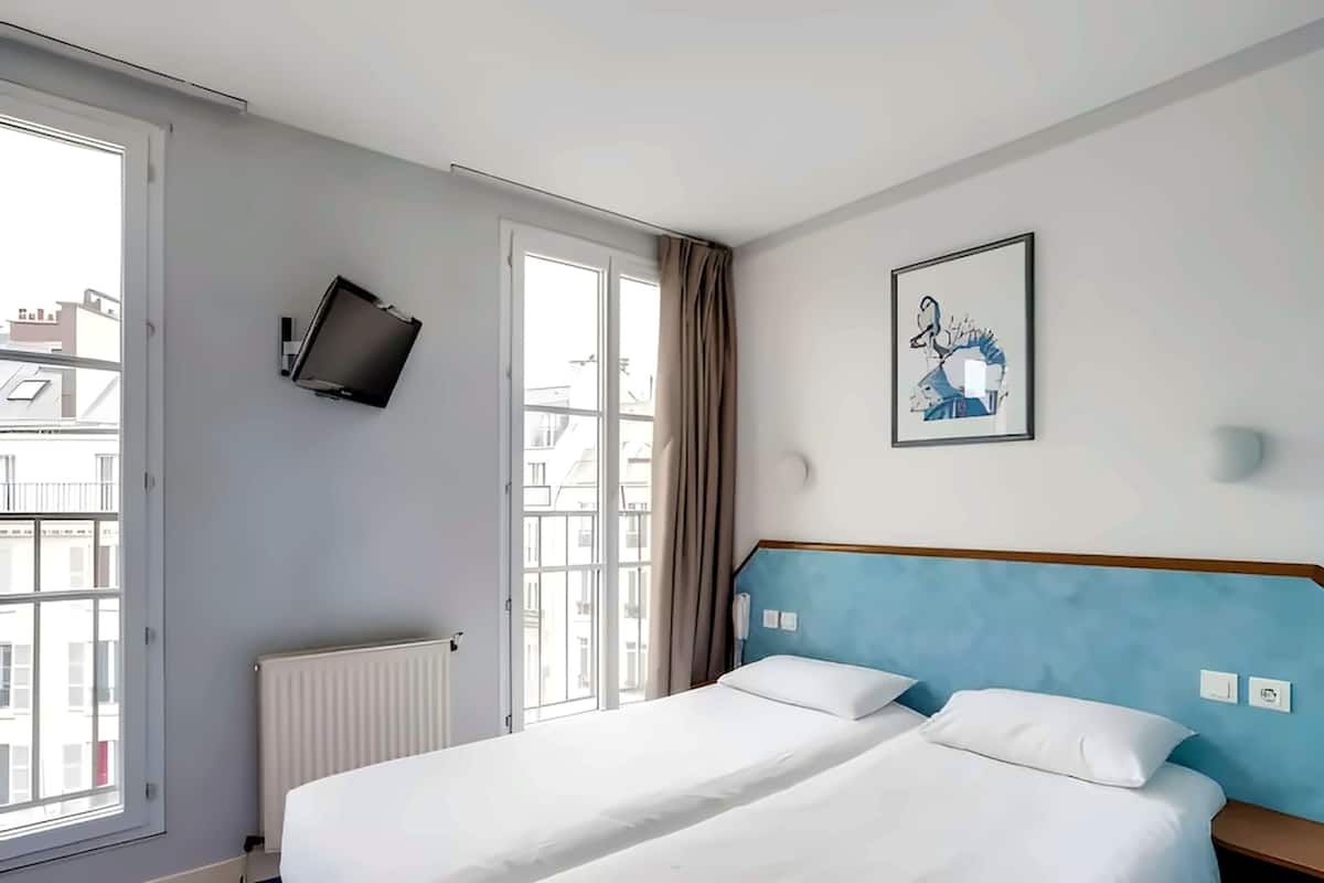 Habitación de hotel con una cama grande, un televisor montado en la pared y una ventana con vista a edificios.