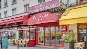 A hotel with a red facade, large glass windows, and outdoor seating.