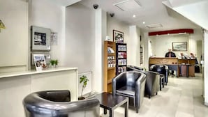 A hotel reception area with a reception desk, black leather chairs, a small plant, and a security camera.