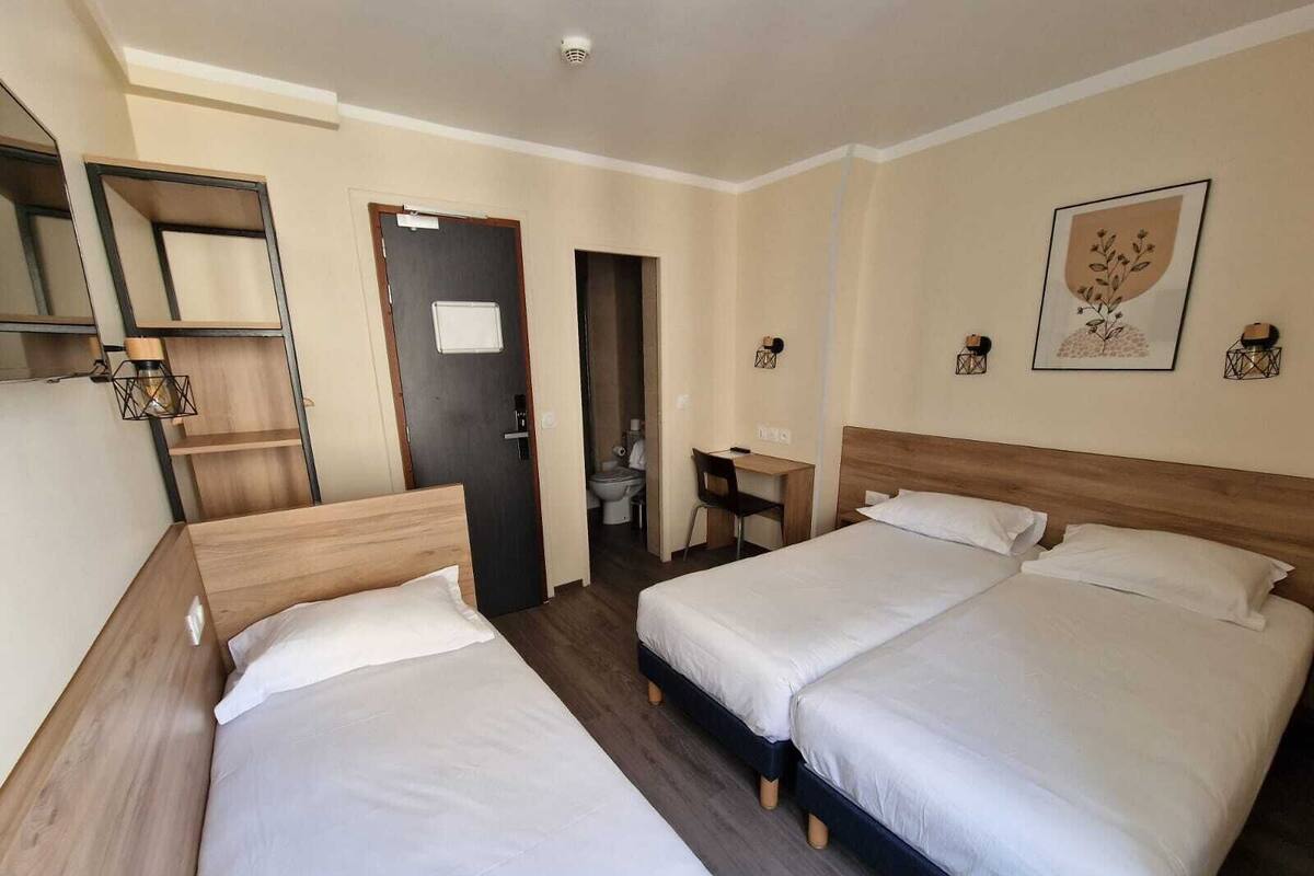 Une chambre d’hôtel avec deux lits, un bureau, une chaise et une petite salle de bain.