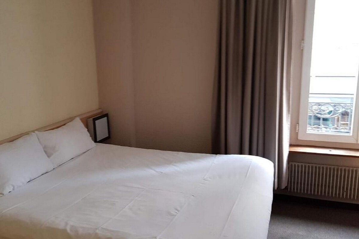 Un lit bien fait dans une chambre d’hôtel, avec une fenêtre et des rideaux.