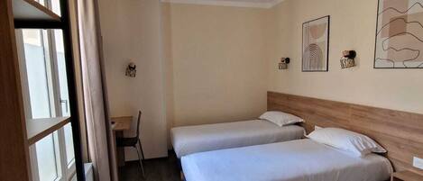 A hotel room with two single beds, a desk, and a chair.