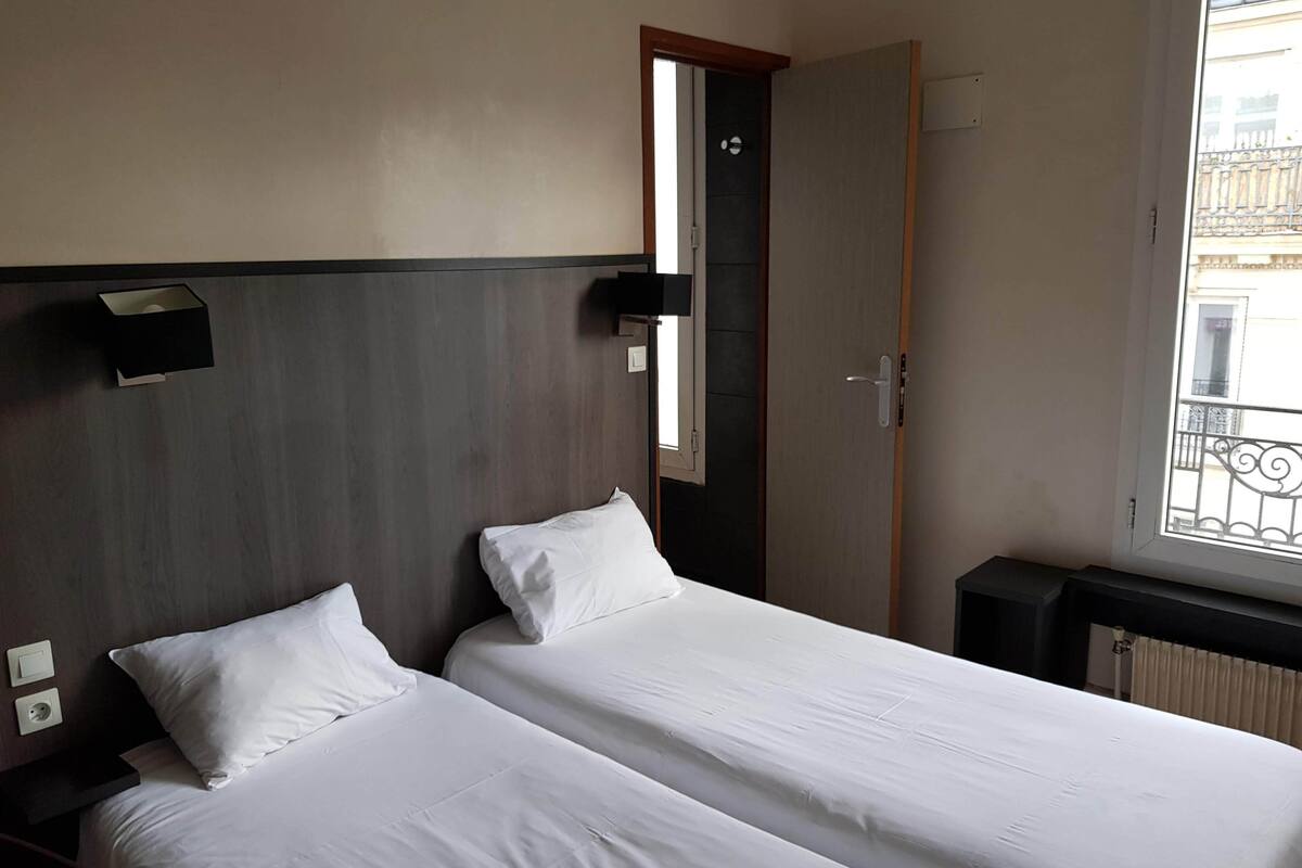 Une chambre d’hôtel avec deux lits, une fenêtre donnant sur un paysage agréable, une porte et un luminaire fixé au mur.